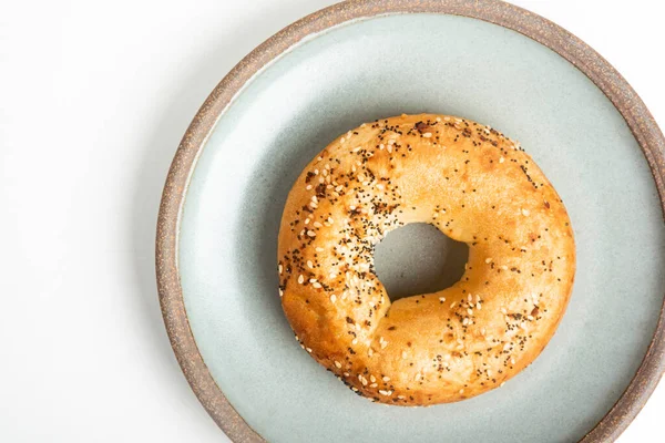 Beyaz arka planda seramik tabakta taze pişmiş tek bir simit..