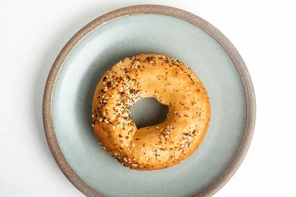 Beyaz arka planda seramik tabakta taze pişmiş tek bir simit..