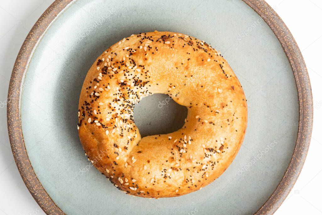 A single freshly baked bagel on a ceramic plate set on a plain white background.