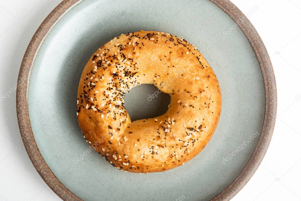 A single freshly baked bagel on a ceramic plate set on a plain white background.