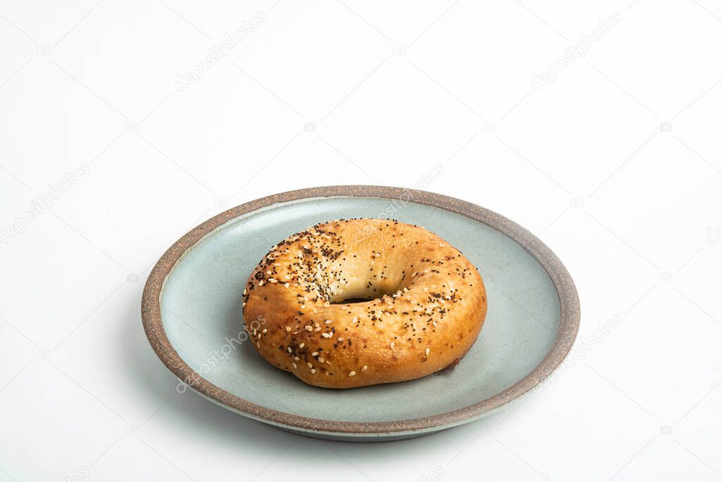 A single freshly baked bagel on a ceramic plate set on a plain white background.