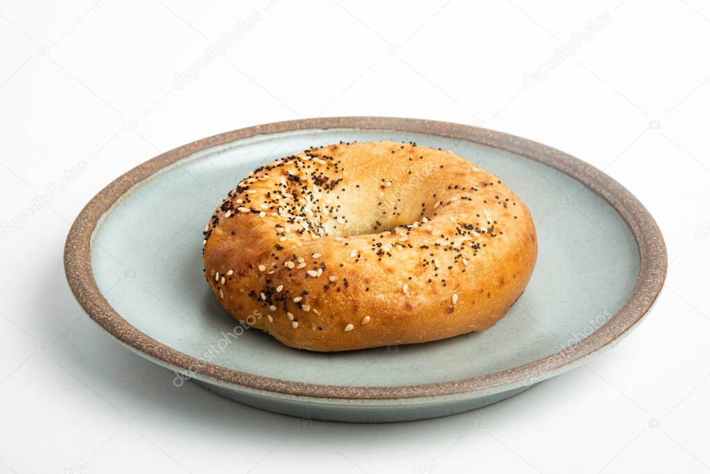 A single freshly baked bagel on a ceramic plate set on a plain white background.