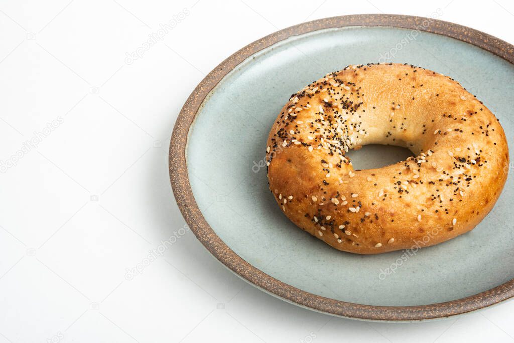 A single freshly baked bagel on a ceramic plate set on a plain white background.