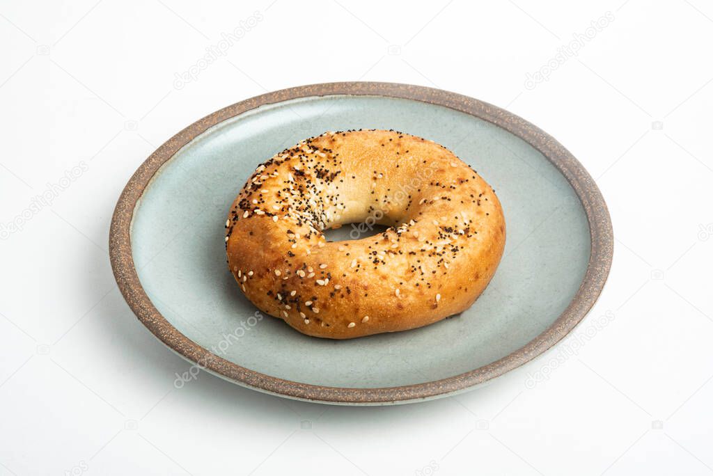 A single freshly baked bagel on a ceramic plate set on a plain white background.