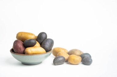 An assorted color raw and fresh potatoes artfully arranged on bowl and table set on plain white background. clipart