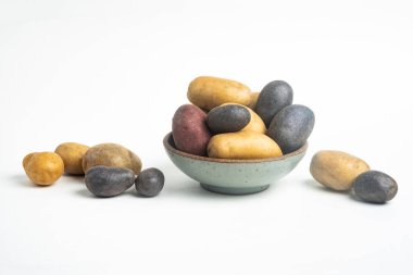 Çeşit çeşit renkte çiğ ve taze patatesler, sade beyaz arka plandaki kasede ve masada ustalıkla düzenlenmiştir..