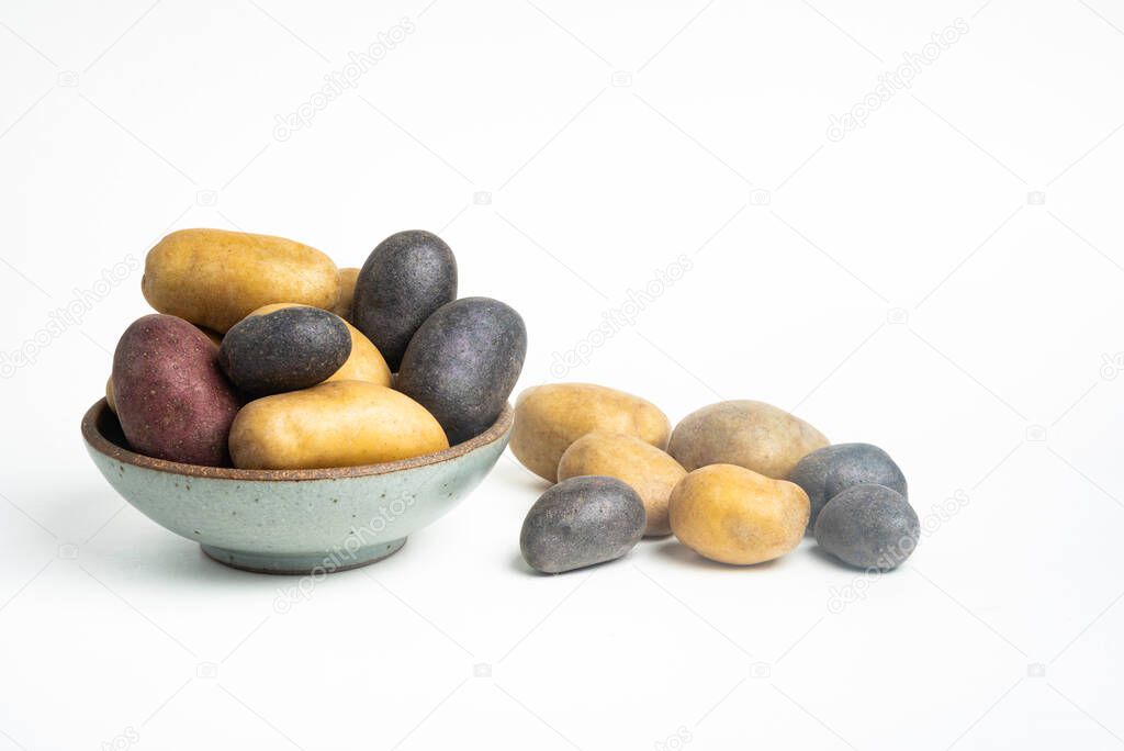 An assorted color raw and fresh potatoes artfully arranged on bowl and table set on plain white background.