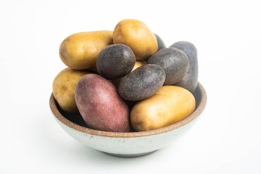 Çeşitli renkte çiğ ve taze patatesler bir kasede ustalıkla yerleştirilmiş ve beyaz arka planda ayarlanmış..