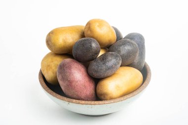 Çeşitli renkte çiğ ve taze patatesler bir kasede ustalıkla yerleştirilmiş ve beyaz arka planda ayarlanmış..