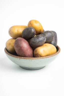 Çeşitli renkte çiğ ve taze patatesler bir kasede ustalıkla yerleştirilmiş ve beyaz arka planda ayarlanmış..