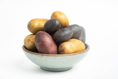 Çeşitli renkte çiğ ve taze patatesler bir kasede ustalıkla yerleştirilmiş ve beyaz arka planda ayarlanmış..