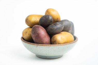 Çeşitli renkte çiğ ve taze patatesler bir kasede ustalıkla yerleştirilmiş ve beyaz arka planda ayarlanmış..