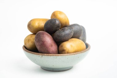 Çeşitli renkte çiğ ve taze patatesler bir kasede ustalıkla yerleştirilmiş ve beyaz arka planda ayarlanmış..