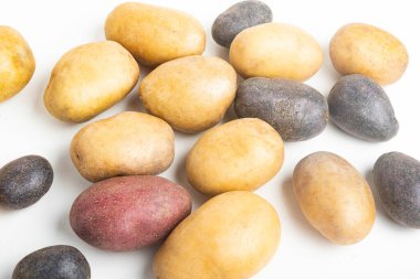 An assorted color raw and fresh potatoes artfully arranged and set on flat white surface table background. clipart