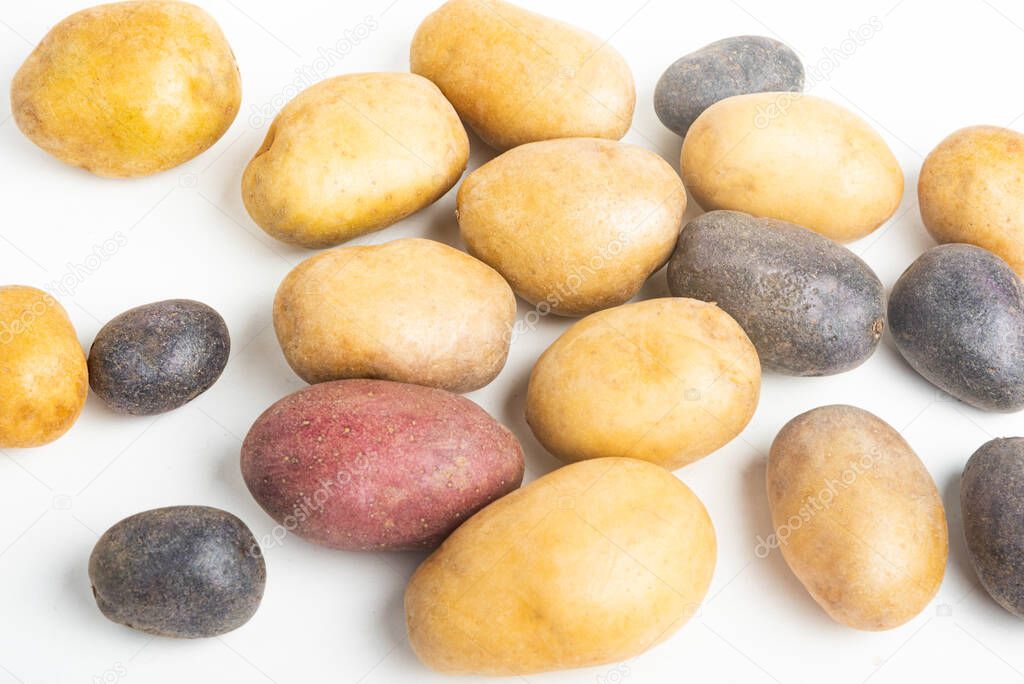 An assorted color raw and fresh potatoes artfully arranged and set on flat white surface table background.