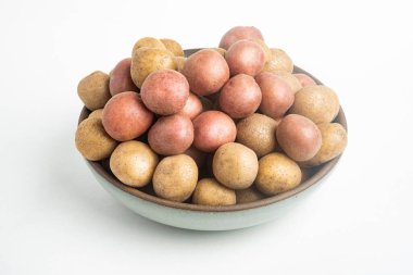 Çiğ ve taze bebek patatesler ustalıkla bir kaseye konulmuş ve beyaz arka plan üzerine kurulmuş..