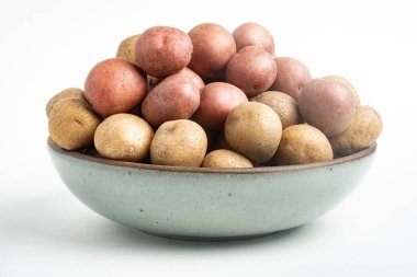Çiğ ve taze bebek patatesler ustalıkla bir kaseye konulmuş ve beyaz arka plan üzerine kurulmuş..