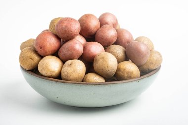 Çiğ ve taze bebek patatesler ustalıkla bir kaseye konulmuş ve beyaz arka plan üzerine kurulmuş..