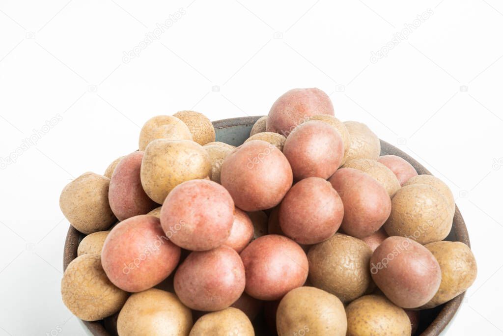 Raw and fresh baby potatoes artfully arranged in a bowl and set on white background.