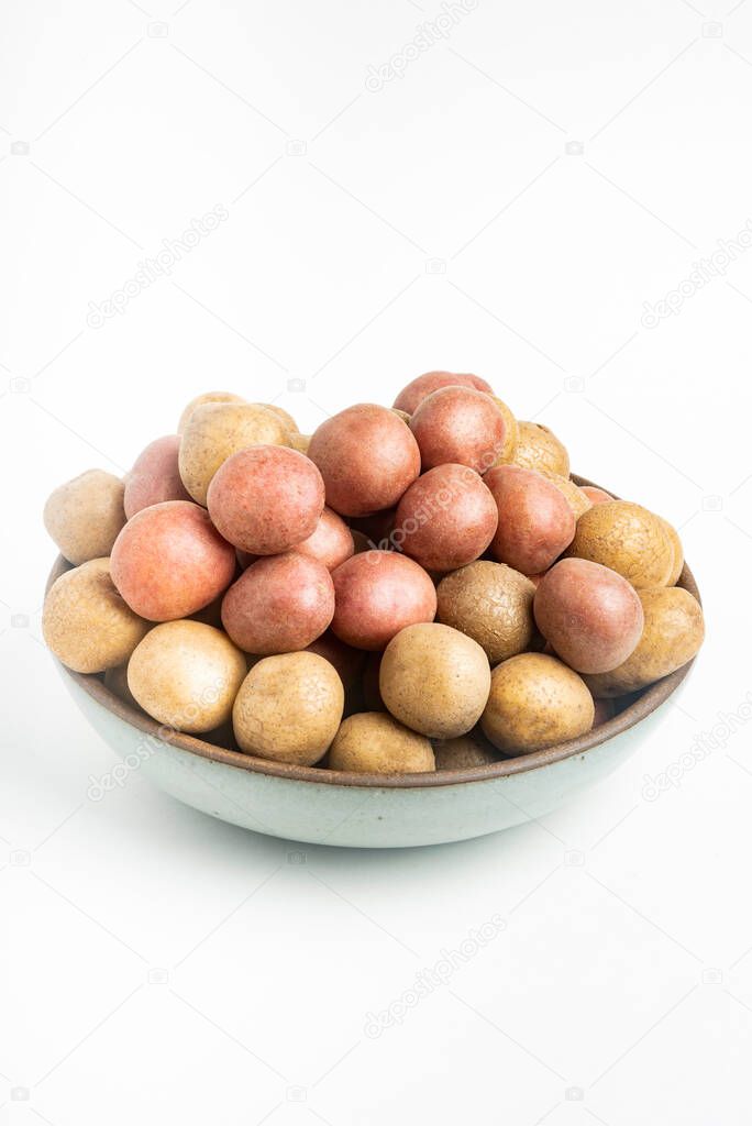 Raw and fresh baby potatoes artfully arranged in a bowl and set on white background.