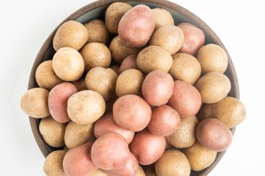 Çiğ ve taze patateslerin üst görüntüsü bir kasede ustalıkla düzenlenmiş ve beyaz arka planda ayarlanmış..