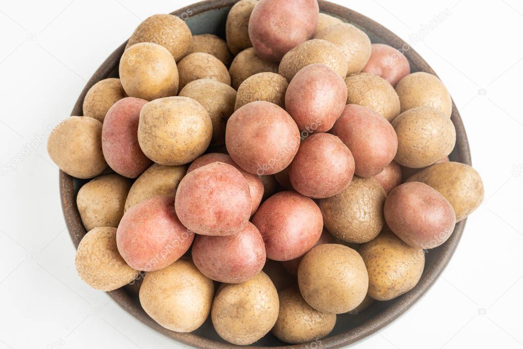 Top view of raw and fresh baby potatoes artfully arranged in a bowl and set on white background.