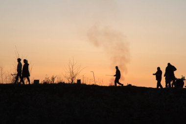 Kırmızı gökyüzünün arka planında insanların siluetleri. Deniz kıyısında gün batımı, insanlar bir tepede yürüyorlar. Akşam. Bahar.
