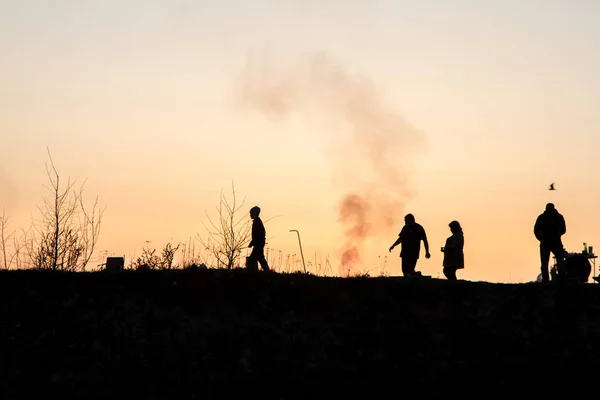 Silhouettes of people on a background of red sky. Sunset on the seashore, people are walking on a hill. Evening. Spring.