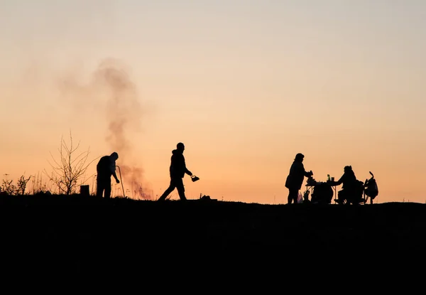 The main theme of this photo is the shadow and silhouettes of people against the backdrop of the sunset. Sunset on the bay. People relax, walk. Family roasts meat.