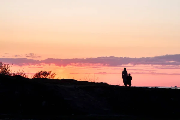 Silhouettes of people on a background of red sky. Sunset on the seashore, people are walking on a hill. Evening. Spring.