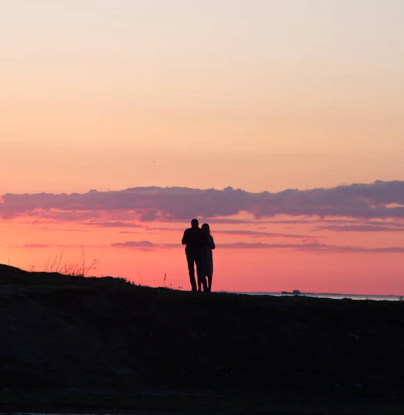 Silhouettes of people on a background of red sky. Sunset on the seashore, people are walking on a hill. Evening. Spring.