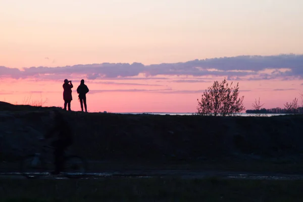 Silhouettes of people on a background of red sky. Sunset on the seashore, people are walking on a hill. Evening. Spring.