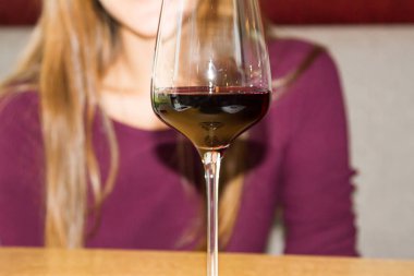 Tahta bir masada bir kadeh kırmızı şarap. Genç bir kız bir kafede oturuyor. Bir kıpkırmızı atış.