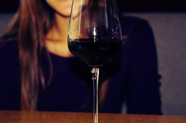 Tahta bir masada bir kadeh kırmızı şarap. Genç bir kız bir kafede oturuyor. Bir kıpkırmızı atış.