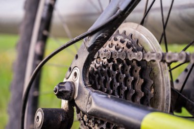 Bisikletin arka tekerleğinin bir görüntüsü. Vites kayması ve zincir görülebilir. Akşam, bahar, bulutlu.