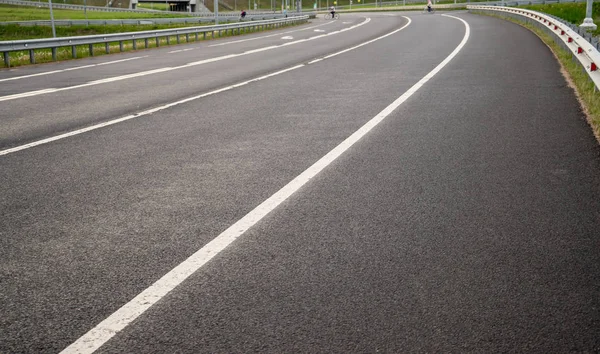 Asphalt road, two-lane. Exit from the highway. White markings on two strips. Metal bump with red reflectors. Cloudy day, spring, evening.