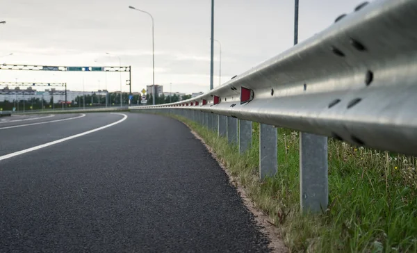 Asphalt road, two-lane. Exit from the highway. White markings on two strips. Metal bump with red reflectors. Cloudy day, spring, evening.