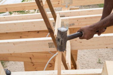 İşçiler, marangozlar, balyozla tahta iğneler çekiçlemeler. Ahşap bir evin detayları. Tavan kirişleri ve yapıştırılmış lamine ahşap evin duvarları. Yaz günü.