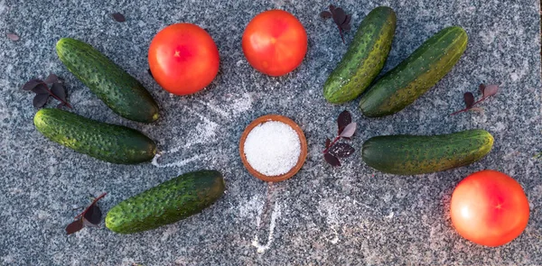 A collage of fresh vegetables on the background of a granite boulder. A collage of red tomatoes, green cucumbers, salt lying on a stone. Summer, evening, fresh air.