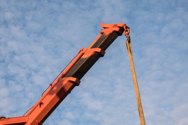 Mavi gökyüzüne karşı kırmızı vinç patlaması. Araba manipülatör boruyu boşaltıyor. İnşaat işleri. Yaz. Güneşli bir gün.