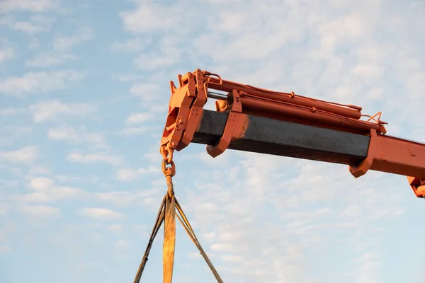 Red crane boom against the blue sky. Car manipulator unloads the pipe. Construction works. Summer. Sunny day.