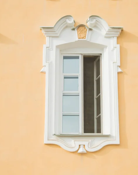 Window of an old building, palace. The frame is made of stucco in the Baroque style. White linen on a yellow background of the walls (ocher). Grand Peterhof Palace. Summer is a sunny day.