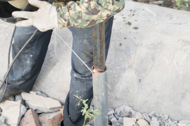 Kaynakçı işte. Kaynak makinesi kullanılarak metal bir kolon montajı. Elektrotlardan kıvılcımlar. Yaz. Gün.