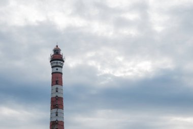 Gökyüzüne karşı renkli deniz feneri. Gemilere, teknelere, yatlara, yelkenlilere, su taşımacılığına ışık sinyalleri göndermek için fenerli eski bir kule. Oryantasyon için tasarlanmış, tehlike uyarır. Deniz kıyısında, okyanusta, gölde inşa edilmiş. Yaz, gün, bulutlu.