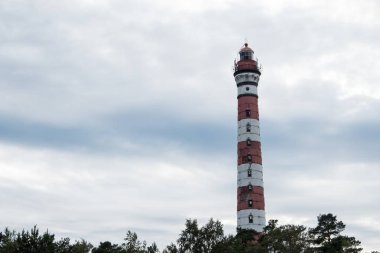 Gökyüzüne karşı renkli deniz feneri. Gemilere, teknelere, yatlara, yelkenlilere, su taşımacılığına ışık sinyalleri göndermek için fenerli eski bir kule. Oryantasyon için tasarlanmış, tehlike uyarır. Deniz kıyısında, okyanusta, gölde inşa edilmiş. Yaz, gün, bulutlu.