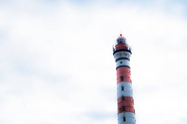 Gökyüzüne karşı renkli deniz feneri. Gemilere, teknelere, yatlara, yelkenlilere, su taşımacılığına ışık sinyalleri göndermek için fenerli eski bir kule. Oryantasyon için tasarlanmış, tehlike uyarır. Deniz kıyısında, okyanusta, gölde inşa edilmiş. Yaz, gün, bulutlu.