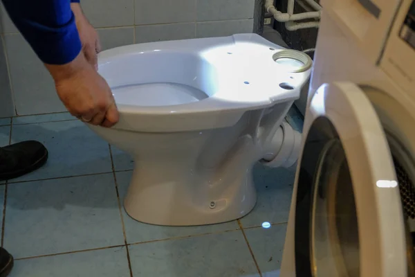 Bir tesisatçı işçisi yeni bir tuvalet kuruyor. Banyoda yeni, beyaz, porselen tuvalet.