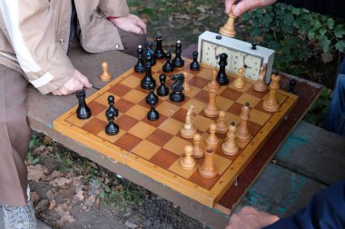 İki adam satranç oynar. Tahta bir tahta üzerinde ahşap satranç taşları. Partinin başlangıcı, ilk. Oyun zamana karşı gerçekleşir. Park bankı. Sonbahar günü.