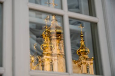 Penceredeki Ortodoks Kilisesi'nin yansıması. Peterhof'taki Büyük Saray'ın altın kubbeleri ve haçları. Mavi gökyüzüne karşı altın parıltısı. Sonbahar güneşli gün.