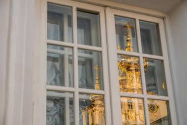Penceredeki Ortodoks Kilisesi'nin yansıması. Peterhof'taki Büyük Saray'ın altın kubbeleri ve haçları. Mavi gökyüzüne karşı altın parıltısı. Sonbahar güneşli gün.